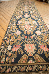 Long angled view of an antique Karabagh rug runner's floral bouquets in pink and bronze on a navy field.