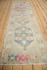 Distressed Oushak runner's machine-bound edge with cream, magenta, and dusty teal geometric patterns.
