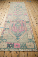 Distressed Oushak runner with repeating geometric motifs and faded cream, pink, and teal hues.