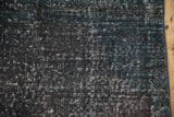 Distressed vintage overdyed rug pile showing charcoal, dark teal tones, and bound edge.