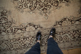Overhead view of a distressed Tabriz carpet's low-pile texture and chocolate brown arabesque details.
