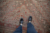 Distressed Khotan carpet, muted red floral pinwheel motifs, oxidized silver tones underfoot.