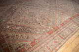 Distressed Khotan rug with muted brick red floral pinwheel field and patterned border.