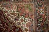 Distressed Heriz carpet corner displaying serrated outlines, vines, and florals in burgundy, green, and pale blue.