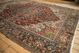 Distressed vintage Heriz rug corner featuring curvilinear floral patterns, rich tones, and white fringe.