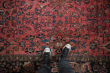 Feet on vintage Lilihan carpet, dusty red floral field, scattered white knots, dark navy border.