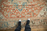Low-pile texture of a distressed Heriz carpet with geometric terracotta and dusty blue floral motifs.