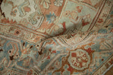 Folded vintage Heriz carpet showing the textured, worn pile in terracotta and dusty blue.