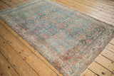 Distressed vintage Hamadan rug corner, faded blue and rust geometric Herati pattern, border visible.