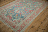 Angled view of a distressed Malayer rug with faded raspberry floral patterns on a denim blue field.