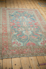 Angled view of a distressed Malayer rug with faded raspberry botehs on a time-softened denim blue field.