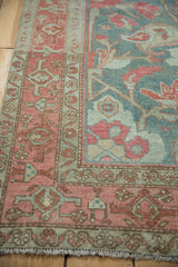 Angled corner view of a distressed Malayer rug showing the raspberry border beside the denim blue paisley field.