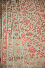 Angled view of an antique Khotan rug's geometric border and coral pomegranate field.