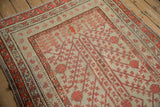 Multiple geometric floral borders in coral red and plum on a distressed antique Khotan rug.
