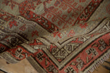 Softly folded antique Khotan rug showing textured wear on its geometric coral and plum borders.