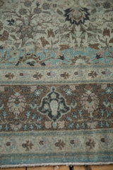 Distressed Qom carpet detail with intricate serrated leaves in aqua, mauve, and brown.