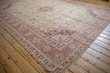 Distressed Oushak rug corner showing ivory and faded raspberry vinery, geometric borders.