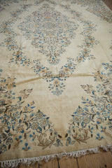 Vintage Kerman carpet with ivory field, blue-gold blossoms, and partial lower fringe.