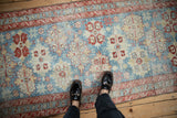 A view from above showing the scale of a distressed Persian runner with serrated red medallions on a powder blue field.