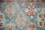 Close-up of the hand-knotted texture, showing red and ivory serrated medallions on a worn powder blue field.