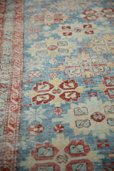 Angled detail of the antique runner's worn pile, highlighting the red wave border and blue field.