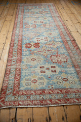 Angled view of a distressed Persian runner with a powder blue field and red reciprocating wave border.