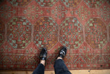 Distressed antique Ersari rug showcasing repeating guls in faded raspberry, blue, and green, underfoot.
