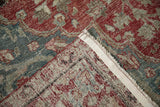 Folded Distressed Khoy carpet showing worn red and teal pile, exposed foundation, secured edge.