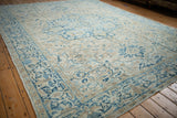 Angled view of a distressed Heriz carpet showing sprawling motifs in blue, sand, and cream.