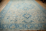 Angled perspective of a vintage distressed Heriz carpet with blue and sand floral patterns.