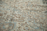 Visible texture of a distressed vintage Heriz rug, showing geometric motifs in dusty blue and warm neutrals.