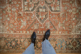 Heriz carpet's geometric pattern in time-softened terracotta and charcoal, showing wear to pile.