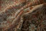 Folds highlighting geometric blossoms, terracotta, charcoal, and soft green abrashes on a vintage Heriz carpet.