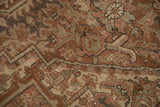 Distressed Persian Heriz rug pile showing geometric arabesques in faded brown, rose, and muted green.