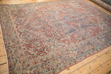 Angled view of a vintage Heriz carpet with low-pile texture and red, blue, and ivory geometric motifs.