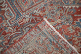 A folded corner reveals the hand-knotted back and distressed pile of a vintage Heriz carpet.
