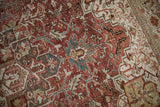 Textured distressed Heriz carpet showing geometric patterns in dusty raspberry, teal, and sand.