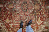 Distressed Heriz carpet with geometric trefoil patterns, abrash, and worn pile texture.