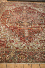 Distressed vintage Heriz carpet segment featuring geometric motifs, serrated finials, brick red tones.