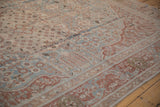 Angled view of the distressed Tabriz carpet's Safavid border and dusty blue floral field.