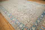 Corner of a distressed vintage carpet with a sapphire blue border and sand-colored floral field.