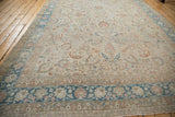 The full length of a distressed Meshed carpet showing its sand-colored field and detailed blue border.