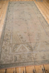Distressed vintage Oushak pile in muted ivory and beige, showing germinating shrub border.