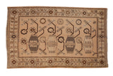 Vintage distressed Khotan carpet with repeating vases and germinating plants on a sandy field.