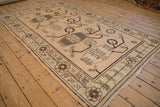Angled view of a distressed Khotan carpet showing its repeating vase and plant pattern in earthy tones.