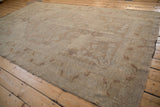Angled view of a distressed Oushak carpet showing its soft, muted beige pattern and worn texture.