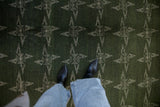 Repeating ivory abstract rose pinwheel pattern on a vintage green Sparta carpet.
