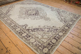 Distressed Oushak rug corner featuring faded aubergine geometric relief and border motifs.