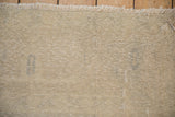 Corner of a distressed Oushak carpet showing its low pile, visible knot heads, and ivory fringe.
