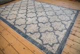 Angled view of a distressed Indian carpet's repeating Moroccan lattice in blue and ivory.